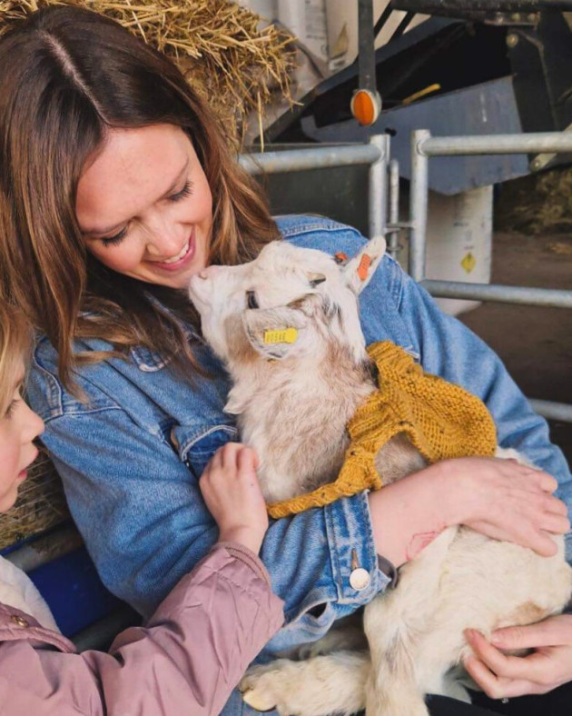A FAMILY CUDDLING A BABY GOAT WEARING A JUMPER