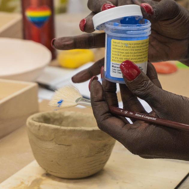 Hands opening a small jar of underglaze to paint with a fan brush.
