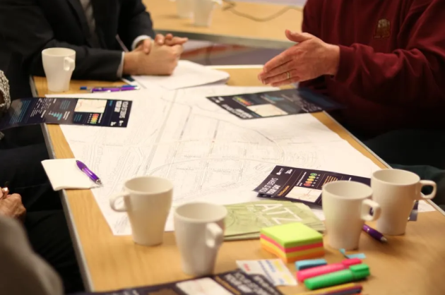 A photo taken at a previous ATZ co-design workshop in St Denys, showing people sat around a table with a large map of the area and various stationary.