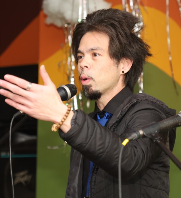 Man reads poetry into a microphone. Photo credit goes to ASTP Photography.