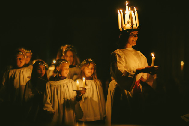 A woman dressed in white and wearing a crown of lit candles on her head leads a parade of young choristers