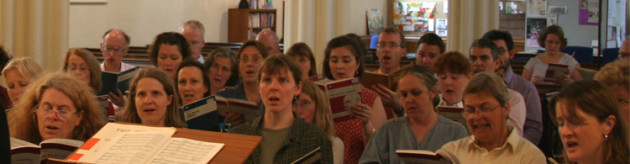 Choir members sitting and singing in rehearsal