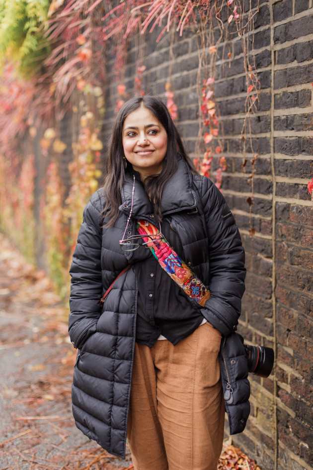 Sujata Setia posing outdoors in front of a wall with vegetation.