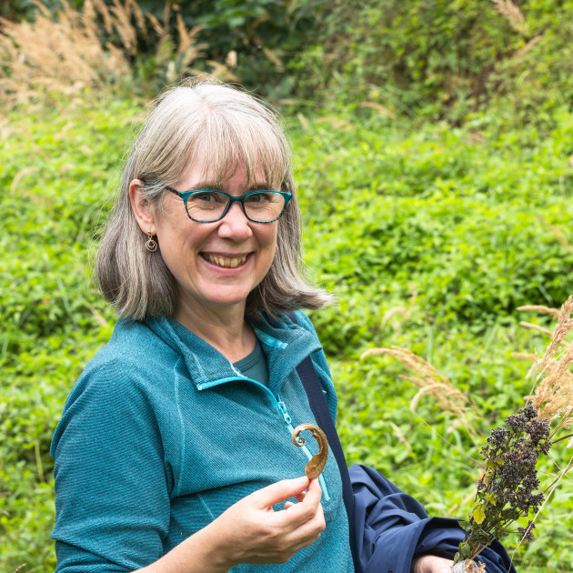Kathryn, standing outside holding a leaf in one hand and some grasses in the other. Behind her is a